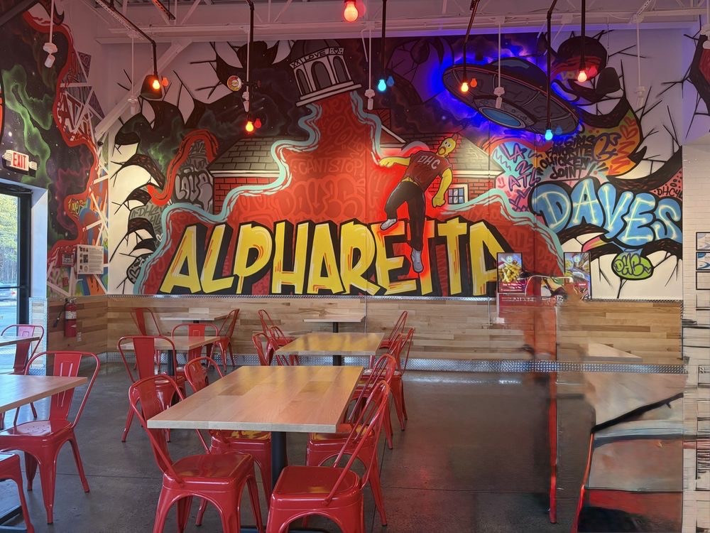 Inside the Alpharetta Dave's Hot Chicken with red chairs and a wall mural
